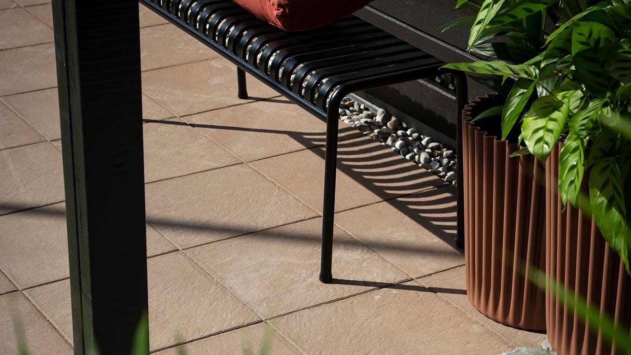 Nærbilde av steinheller i varm fargetone på uteplass med sittebenk.