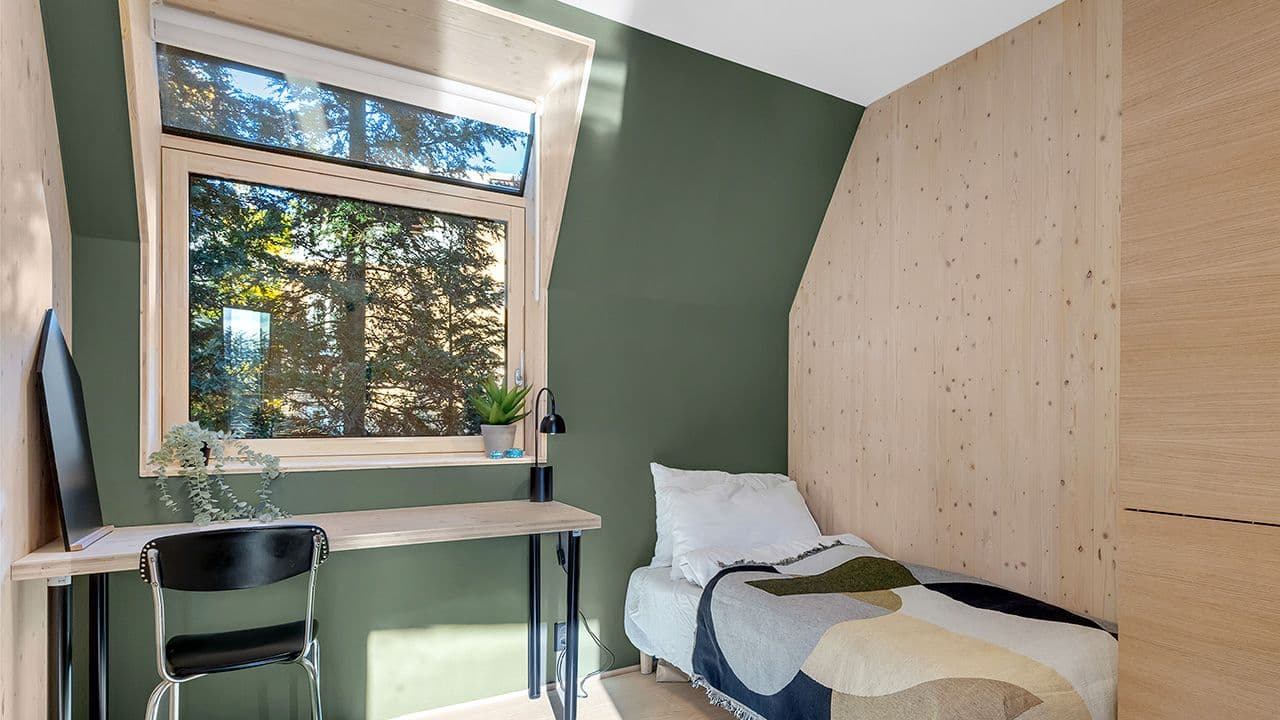 Soverom med grønne vegger, seng og pult med innadslående vindu