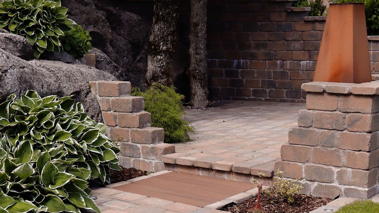 Belegningsstein og mur som skaper soner i hage.