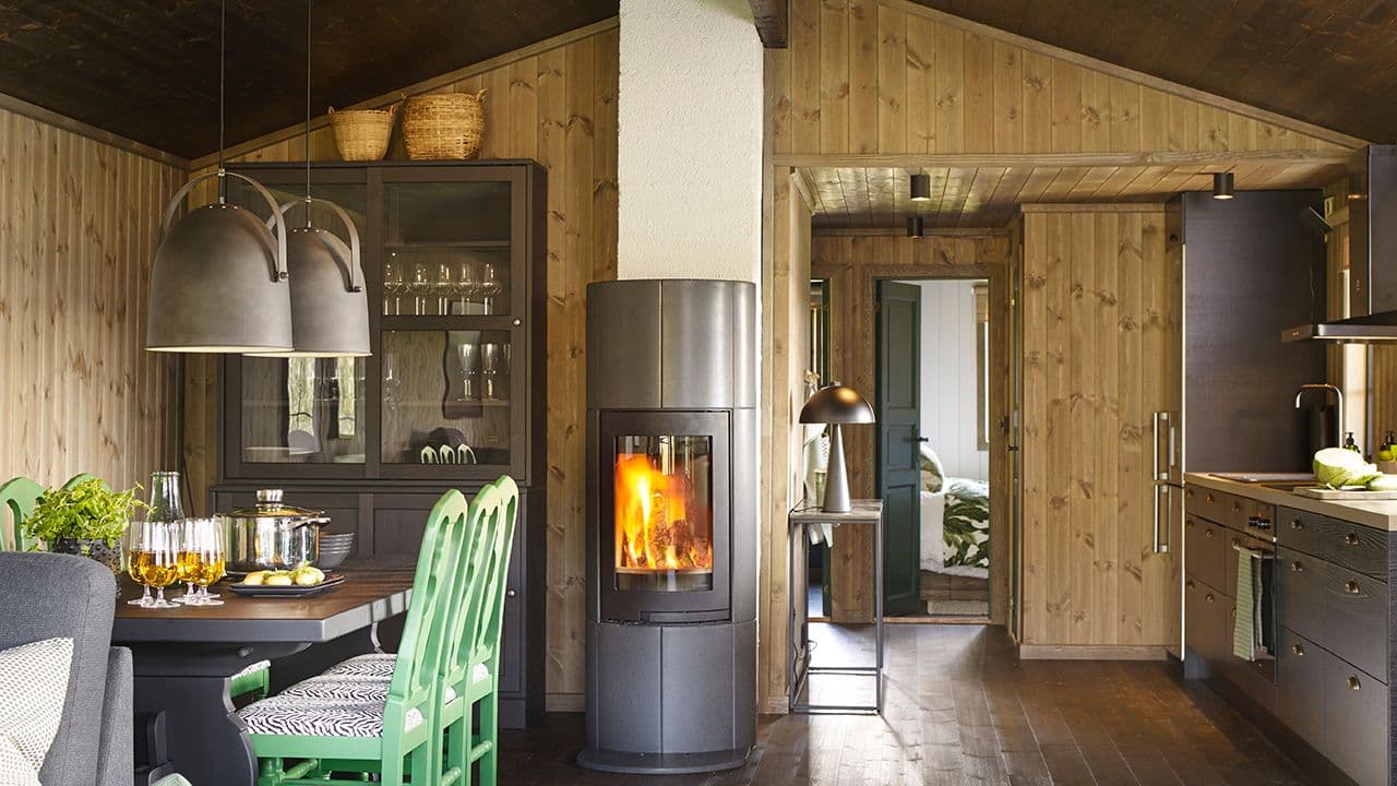 Gammel hytte med mørke panelvegger som er pusset opp med moderne kjøkken, peis og møbler.