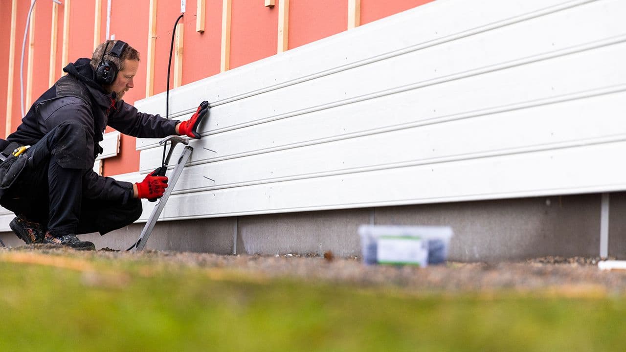 Mann som monterer liggende kledning på gårdshus.