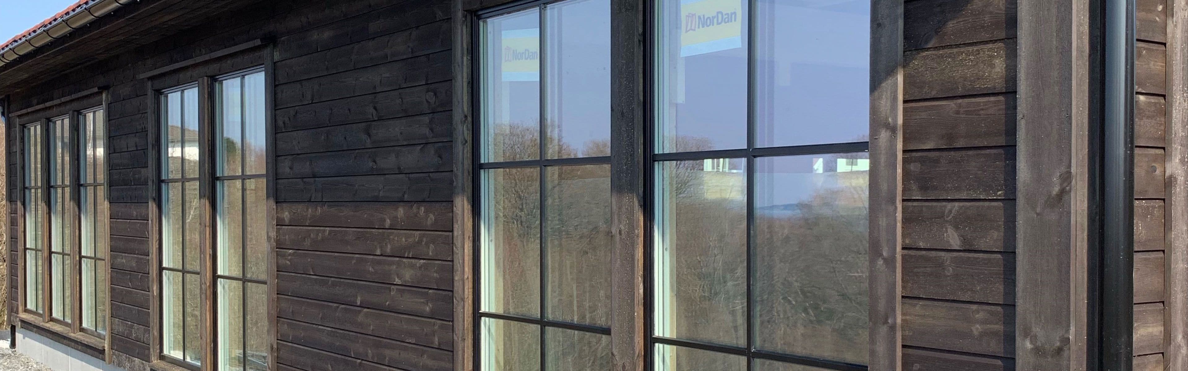 Husvegg med store vinduer og brun kledning med fargede fasadeskruer.