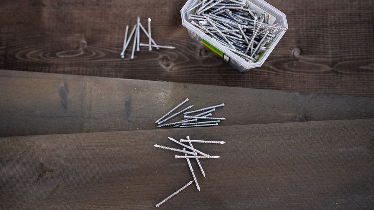 Nærbidle av terrassebord med eske med terrasseskruer og skruer som ligger strødd.