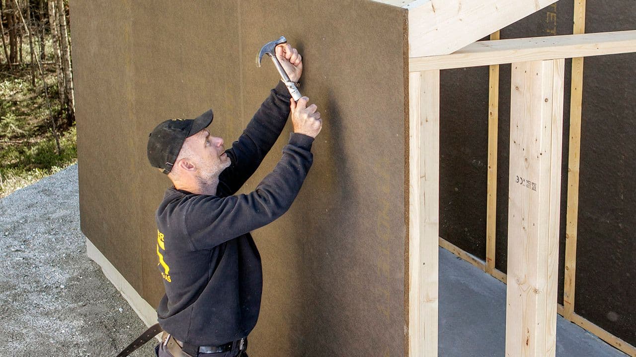Mann som spikrer fast sponplate på vegg.