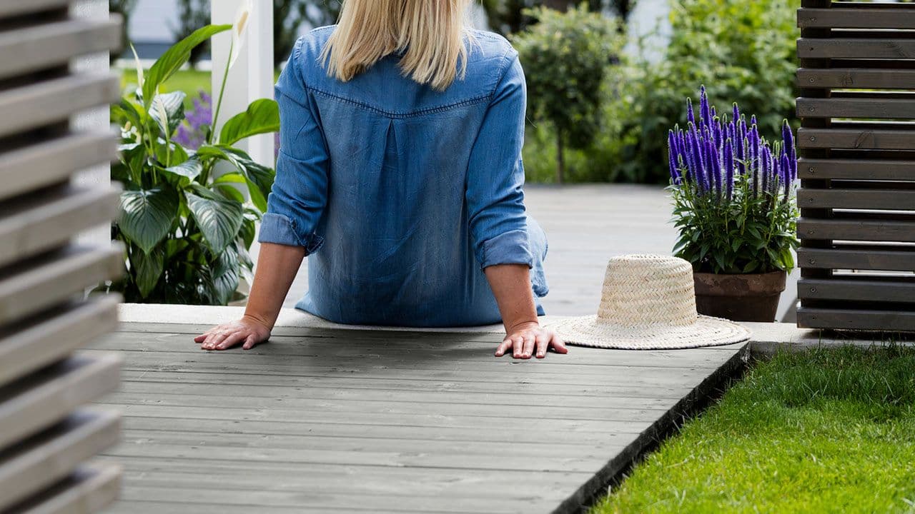 Kvinne som sitter på terrasse beiset med Jotun TREBITT terrassbeis i fargen 90002 Gråsvart og levegg i 0683 Sotgrå.