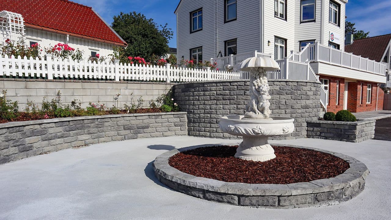 Gårdsplass med fontene, betongtrapp og Aas Tindeblokk støttemur.