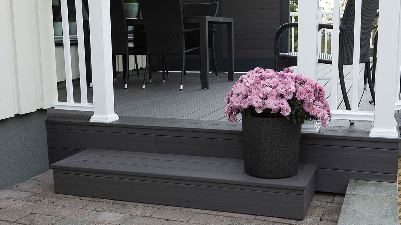 Terrassebord i kompositt på terrasse med trapp med blomsterkrukke med rosa blomster.