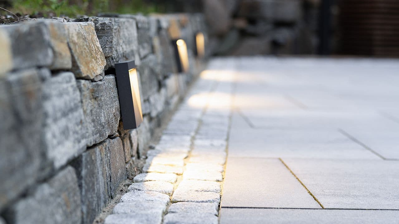 Multiblokk heller lagt sammen med belegningsstein som kant foran steinmur med utebelysning.