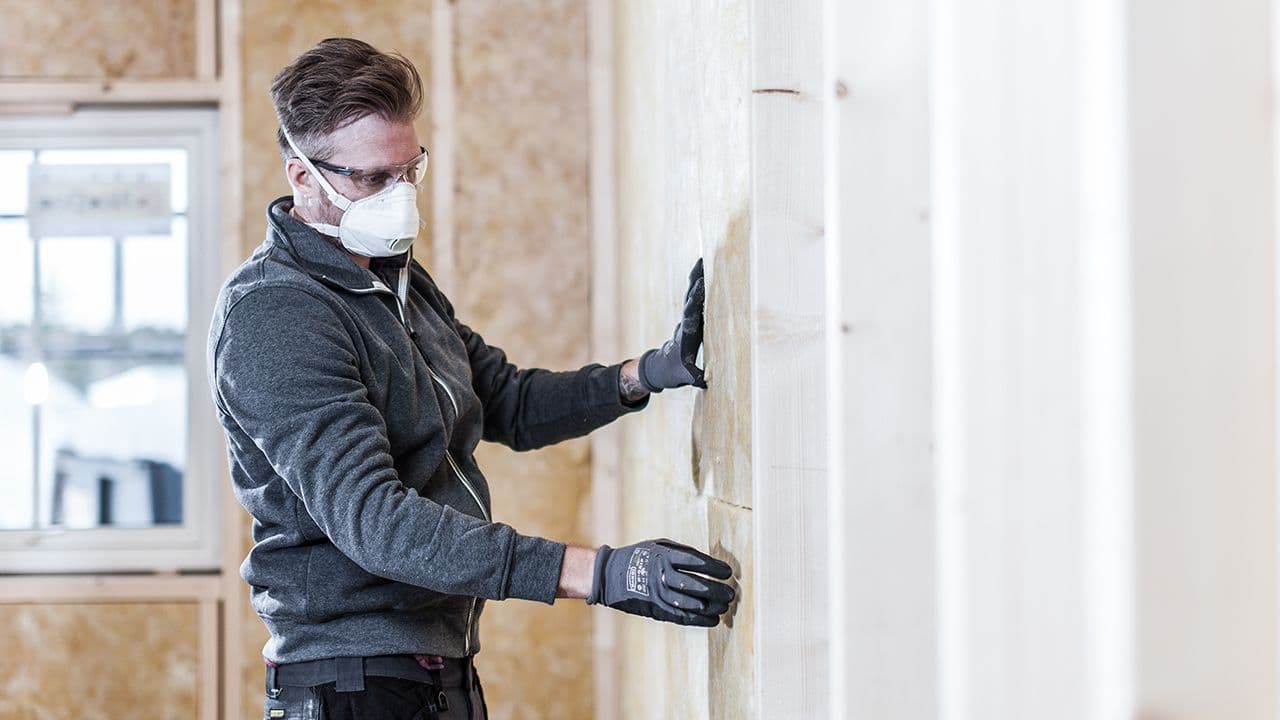 Mann med støvmaske som putter isolasjon i innvendig vegg.