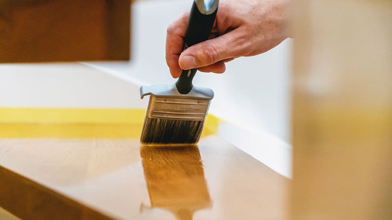 Mann som lakkerer gulv med pensel.