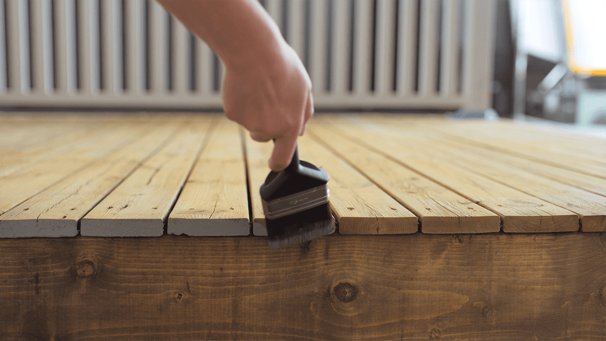 Person som holder på å beise terrassen med pensel.