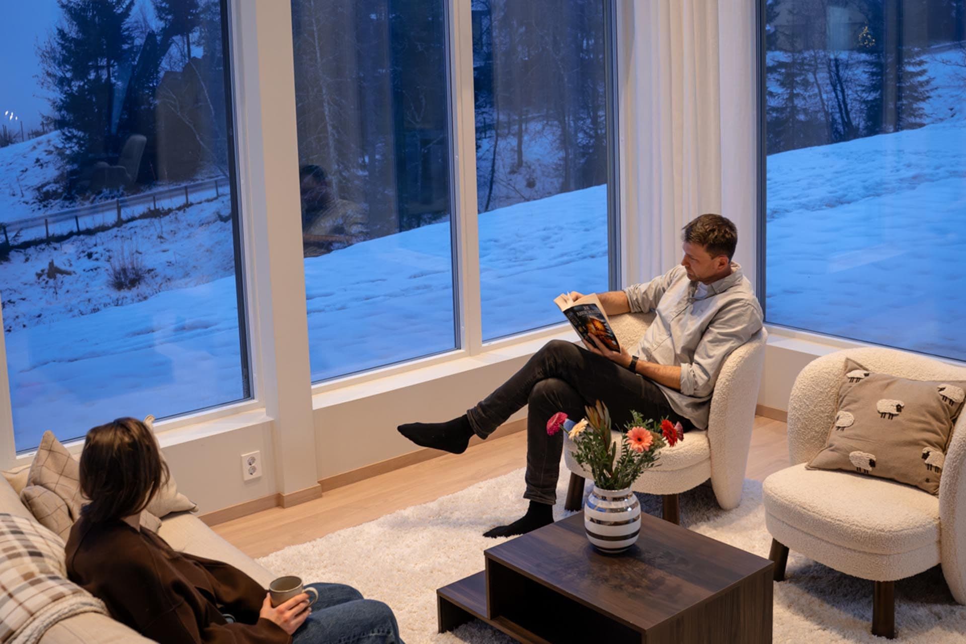 To personer som sitter i en stue med store vinduer.