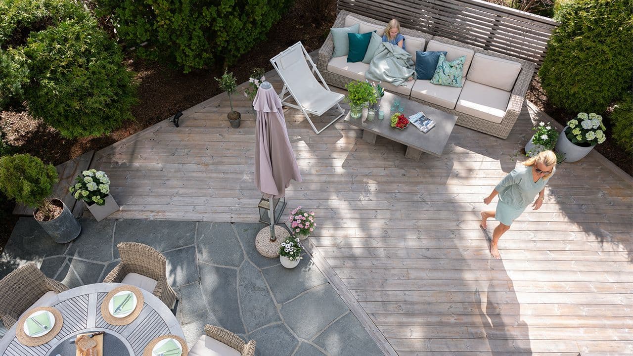 Fugleperspektiv av terrasse i termofuru sammenhengende med skiferstein og levegg i spiler.