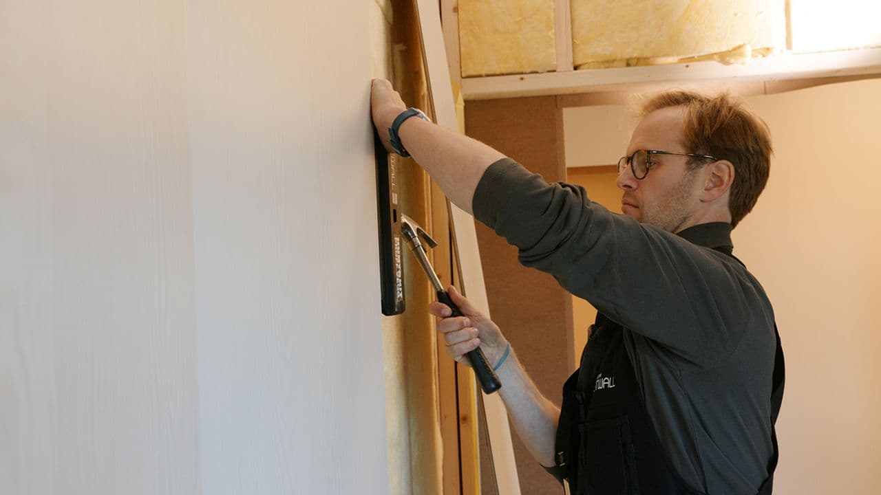 En mann som holder på med montering av MDF veggplater.