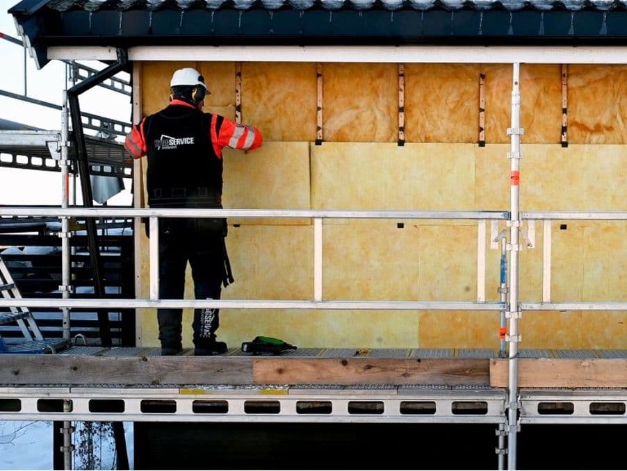 en mann som legger isolasjon utvendig på et hus