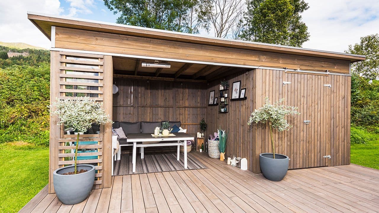 Hage med stor brun hagestue med sittegruppe og utebod.