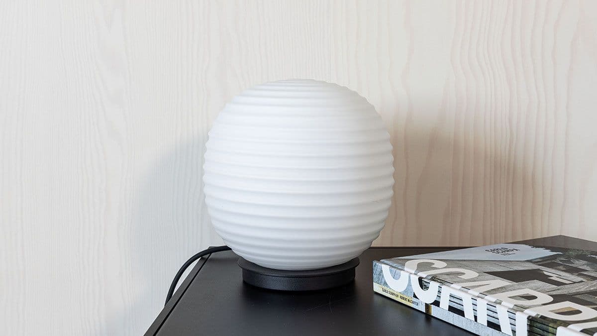 Vegg med smartfiner furu. foran står en rund lampe og et sort bord