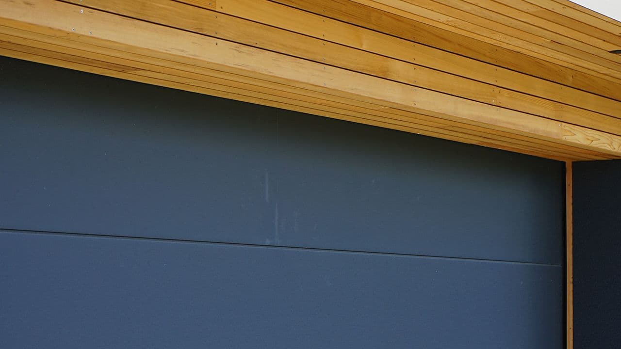 Sort garasjeport til hus med lyst treverk.