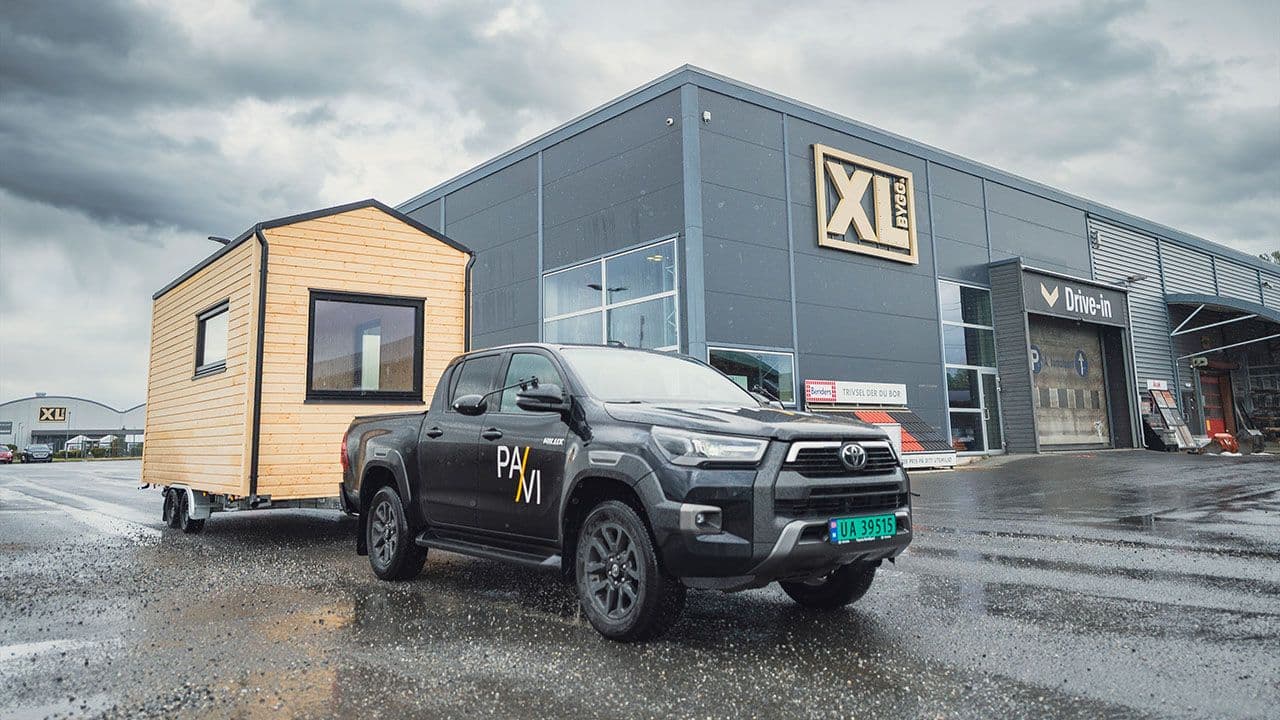 Minihytte på henger etter bil utenfor XL-BYGG varehus.