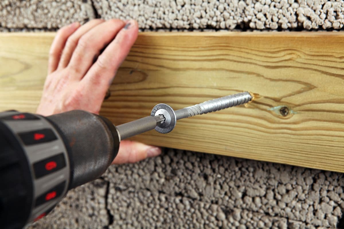 En person fester en stender til en Leca-mur med lettbetongskruer.