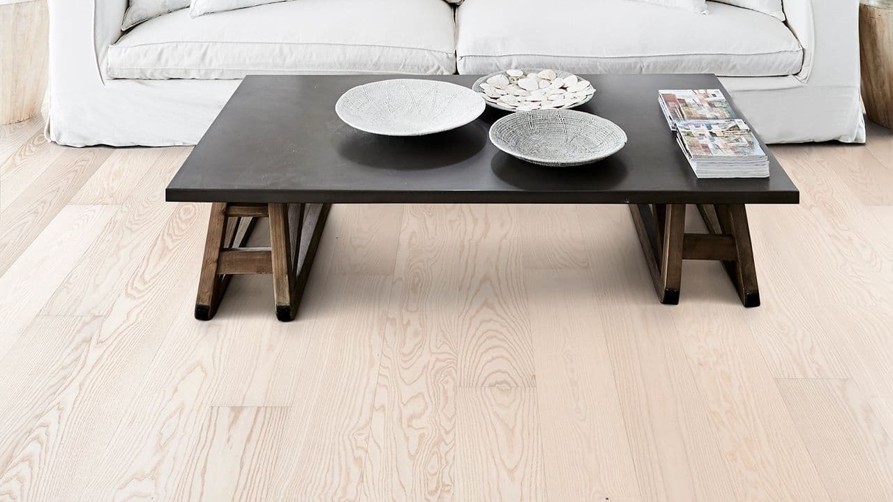 Lyst parkettgulv i ask i stue med lys sofa og mørkt bord.